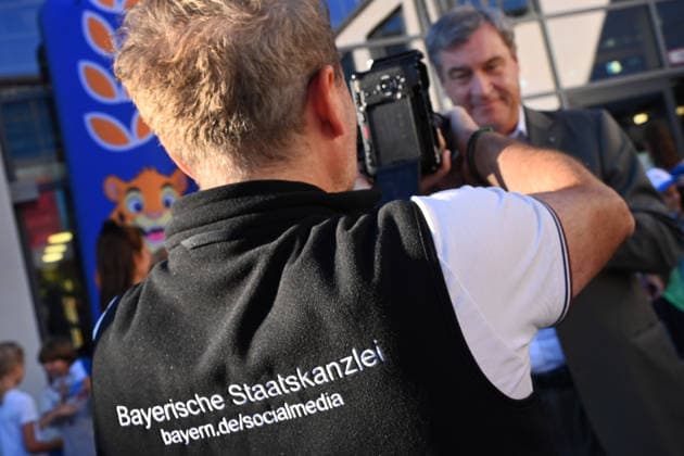 The back of a person with the words Bavarian State Chancellery, Social media takes center stage at a school visit with Minister-President Markus Söder Markus SÖDER, Minister-President of Bavaria and CSU