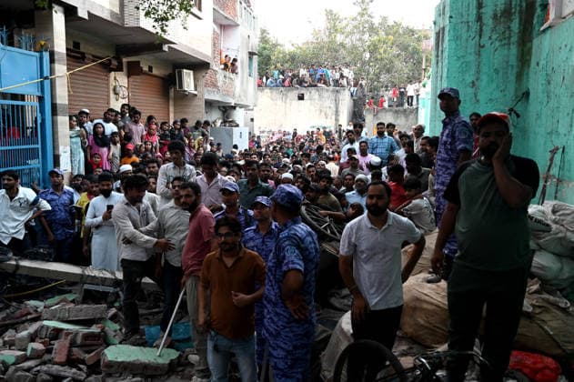 NEW DELHI, INDIA - OCTOBER 7: People look as National Disaster Response Force (NDRF) jawans, Delhi Fire Service personnel, and local residents navigate heavy rubble during a search and rescue operation after a four-storey residential building collapsed in the New Seemapuri area of Shahdara on October 7, 2026, in New Delhi, India. The structural collapse occurred around 3:30 PM behind the local fish market, trapping multiple residents under concrete slabs and damaging two adjoining houses. At least one minor died while eight people were rescued and rushed to Rajiv Gandhi Super Speciality Hospital for emergency medical treatment as sniffer dogs and excavators worked late into the evening to locate remaining trapped survivors. (Photo by Ishant