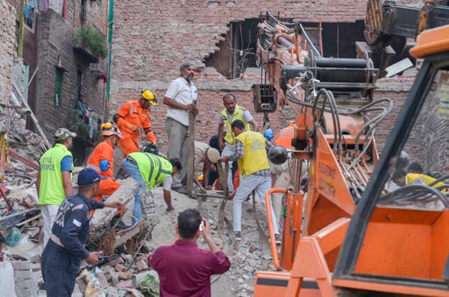 NEW DELHI, INDIA - OCTOBER 7: National Disaster Response Force (NDRF) jawans, Delhi Fire Service personnel, and local residents navigate heavy rubble during a search and rescue operation after a four-storey residential building collapsed in the New Seemapuri area of Shahdara on October 7, 2026, in New Delhi, India. The structural collapse occurred around 3:30 PM behind the local fish market, trapping multiple residents under concrete slabs and damaging two adjoining houses. At least one minor died while eight people were rescued and rushed to Rajiv Gandhi Super Speciality Hospital for emergency medical treatment as sniffer dogs and excavators worked late into the evening to locate remaining trapped survivors. (Photo by Raj K Raj Hindustan T