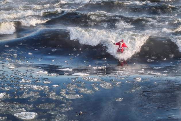 Canada, Surfer dressed as Father Christmas rides a standing wave in the St Lawrence River