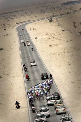 Das Teilnehmerfeld der Tour of Qatar 2006 passiert mit seinem Begleittross eine wüstengesäumte Straße - Radsport Herren Tour of Qatar 2006, Straßenradsport, Straße, Rad, 3. Etappe, Luftaufnahme, Luftbild, Vdig Totale staubig, staubige, Sand, sandig, Öde, karg, karge Doha Weite, Leere,