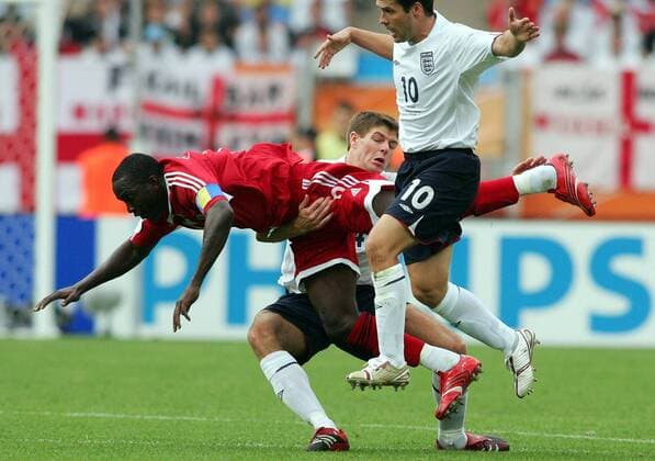 Steven Gerrard (England, hi.) nimmt Dwight Yorke (Trinidad und Tobago) im Zweikampf auf den Arm, re. Michael Owen (England) Fußball Herren WM 2006, Länderspiel, Nationalteam, Gruppe B, Nationaltrikot, England - Trinidad und Tobago 2:0 Gruppe Nürnberg Dynamik, Kampf, Fußball Herren WM 2006, Länderspiel, Nationalteam, Gruppe B, Nationaltrikot, England - Trinidad und Tobago 2:0 Gruppe Nürnberg Dynamik, Kampf,