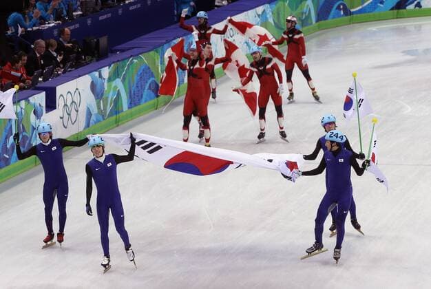 Vancouver , 260210 , Olympische Spiele Vancouver 2010 , Shorttrack , Finale 5000m Männer Staffel, Yoon-Gy Kwak , Ho-Suk Lee , Jung-Su Lee und Si-Bak Sung (Korea, vorn von li.) sowie Olympiasieger Kanada: Charles Hamelin , Francois Hamelin , Olivier Jean und Francois-Louis Tremblay (hi.v.li.) jubeln über den Sieg o0 Fahne, Landesfahne Objekte Südkorea