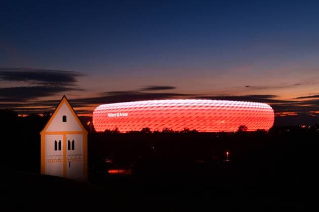 UEFA EURO 2020 in Munich with spectators archive photo ALLIANZ ARENA at night In the foreground a fake church Holy Cross Church Timm Ulrichs, sculpture aVersunkenes Dorfà in Froetttmaninger Berg Dynamic Philips LED lighting provides for flowing transitions in the light animation football arena,football stadium,stadium,FC Bayern Muenchen,night shot,evening sky,night sky,red lighting,red illuminated,light,mood,evening atmosphere,overview,long shot,architecture Â