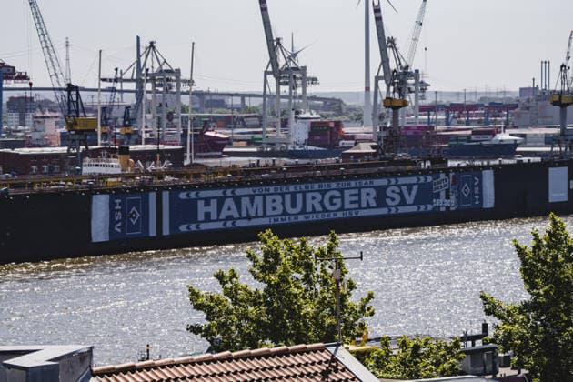 Germany, Hamburg, Port of Hamburg, Blohm Voss Dock 11, Dock 11, floating dock, Hamburger SV, HSV, HSV advertising, member advertising, HSV banner, HSV scarf, soccer culture, traditional club, promotion campaign, Raute Dich de, From the Elbe to the Isar always HSV, Port of Hamburg, Elbe, harbor cranes, container terminal, shipyard, shipyard industry, shipyard, dock facility, maritime scene, Industrial port, port panorama, port operations, shipping, water traffic, container port, port photography, maritime photography, urban photography, northern Germany, city view, industrial architecture, docklands, Elbe view, morning light, sunlight, summer light, Hamburg skyline, port industry, large shipyard, banner advertising, outdoor advertising, logistics, container logistics, wind turbines Copyright: xStefanxTrochax