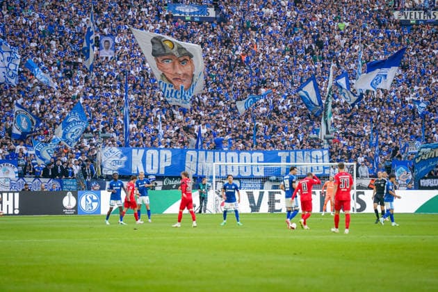 Germany Soccer Bundesliga 2026–2027, Matchday 4: FC Schalke 04 vs. SV Elversberg at Veltins Arena, Gelsenkirchen. FC Schalke 04 fans in the packed North Stand display numerous blue-and-white flags and a large banner reading KOP OMHOOG TIMO ( Keep Your Head Up, Timo ), Timo during the Bundesliga match against SV Elversberg. The specific context of the message cannot currently be reliably verified publicly. North Stand, fans, ultras, fan culture, banner, slogan, solidarity, flags, view from behind the goal, wide shot Copyright: xJOERANxSTEINSIEKx