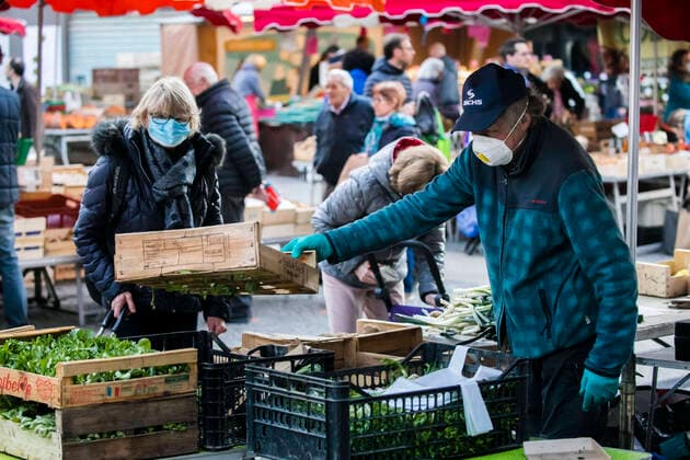 Chambery, France March 21, 2020 - Morning atmosphere at the downtown market during the period of confinement due to the coronavirus health crisis - A saleswoman wearing a sanitary mask serves vegetables to customers EPIDEMIE, CORONAVIRUS, VIRUS, CRISE SANITAIRE, COVID19, VIE QUOTIDIENNE, MARCHE, ALIMENTAIRE, COMMERCANTS, RESTRICTIONS, PANDEMIE, SANTE, AMBIANCE, ATMOSPHERE, CONFINEMENT, INQUIETUDES, FAIRE DES COURSES, RESTRICTIONS DE CIRCULATION, APPROVISIONNEMENT, PRODUITS DE PREMIERE NECESSITE, MALADIE, CHAMBERY, SAVOIE, PROPAGATION DU VIRUS, ALIMENTATION, MASQUE SANITAIRE, LEGUMES Copyright: xVincentxIsorex