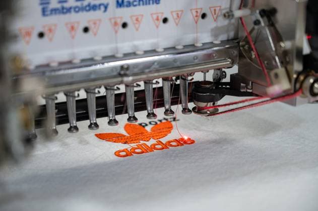 August 6, 2025, New Delhi, Delhi, India: An automatic embroidery machine made in China is stitching an Adidas logo on shoe fabric during the 9th India International Footwear Fair, held at Bharat Mandapam, New Delhi, India. ITPO (India Trade Promotion Organisation) is organizing the 9th edition of the India International Footwear Fair (IIFF) from August 6 to 8, 2025, at Bharat Mandapam. This is a B2B (Business-to-Business) exhibition, showcasing a wide range of products including footwear, synthetic materials, footwear components, accessories, machinery and equipment, and chemicals. Around 250 exhibitors are participating in the fair. New Delhi India - ZUMAs197 20250806_aaa_s197_063 Copyright: xPradeepxGaurx