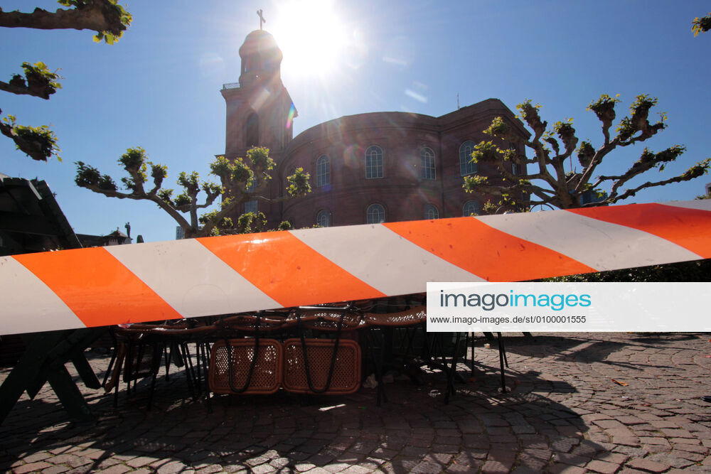 Barrier tape in front of stacked tables and chairs of a closed café s on Paulsplatz in front of the Paulskirche in the most beautiful sunshine in downtown Frankfurt, Hesse, Germany