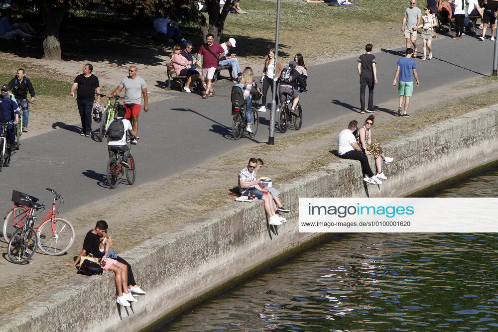 Passers-by enjoy the warm spring day and the sunshine during a walk on the riverbank promenade on the Main in Frankfurt, Hesse, Germany