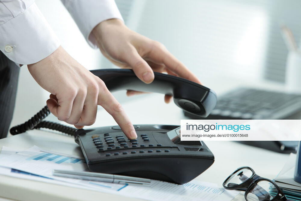 Business Telephone Cropped image of a telephone on a desk with a hand taking the receiver off hook