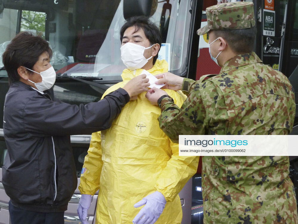 New coronavirus A Japan Ground Self-Defense Force member (R) shows a bus driver how to wear a protective suit at Narita airport, near Tokyo, on April 22, 2020, amid the coronavirus pandemic. Self-Defense Forces personnel are tasked with training bus drivers to transport people who arrived from overseas to hotels without being infected with the coronavirus.