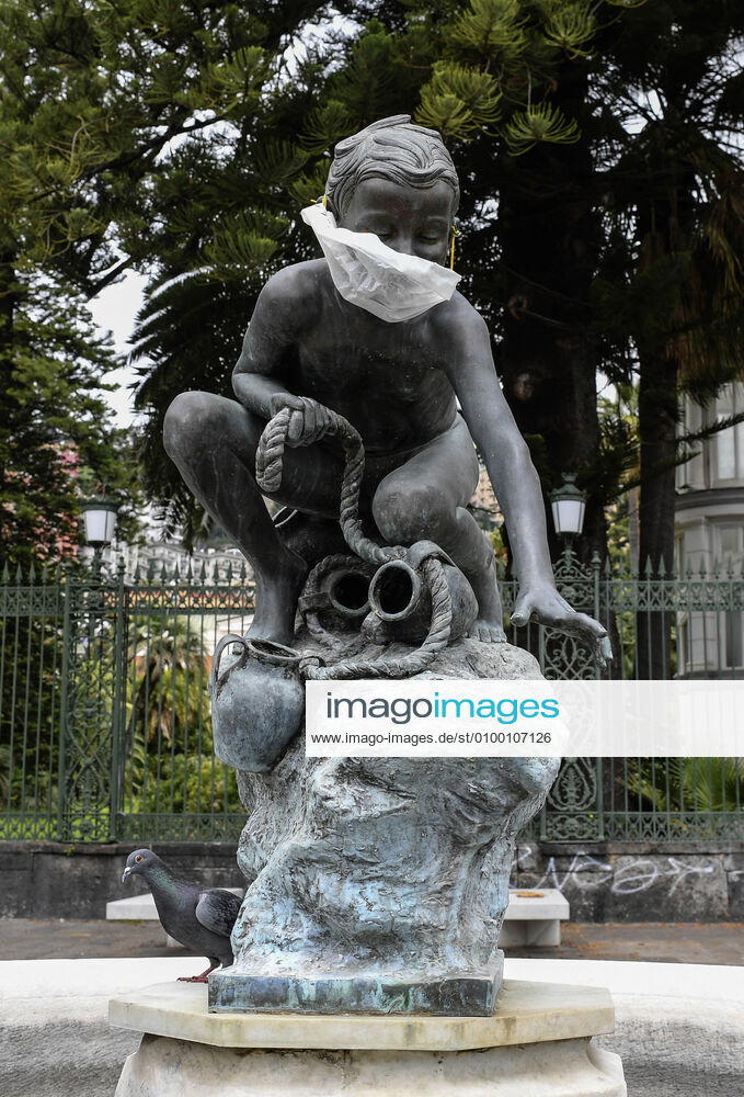 A protective mask is placed on a statue of a child fisherman, in street riviera, in Naples city. Government Decree declaring all of Italy a protected area to combat Covid-19 - Coronavirus infection.