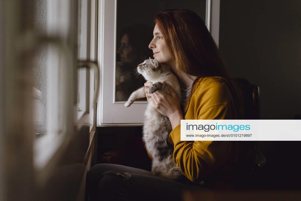 Smiling redheaded woman sitting with her cat at open window at home model released Symbolfoto property released AFVF06224