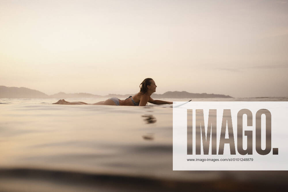 Female surfer lying on surfboard in the evening, Costa Rica model released Symbolfoto HWHF00010