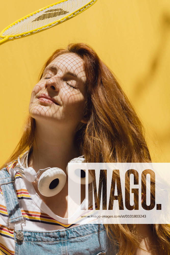 IMAGO Creative, Sommer, Schatten-Plätze bei Hitze Relaxed young woman with badminton racket over face wearing headphones around neck during sunny day model released Symbolfoto property released AFVF06451