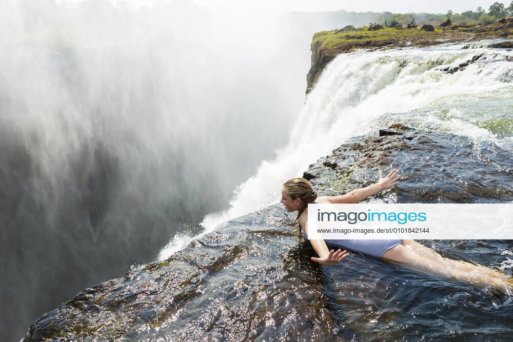 Young girl in the water at the Devils Pool lying on her front, arms spread out, at the edge of the cliff of Victoria Falls. Victoria Falls,Zambia,Young girl in the water at the Devils Pool lying on her front, arms spread out, at the edge of the cliff of Victoria Falls. Young girl in the water at the Devils Pool lying on her front, arms spread out, at the edge of the cliff of Victoria Falls.