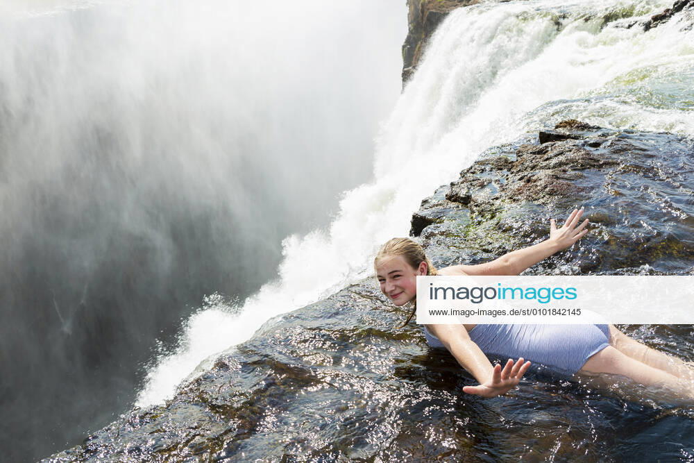 Young girl in the water at the Devils Pool lying on her front, arms spread out, at the edge of the cliff of Victoria Falls. Victoria Falls,Zambia,Young girl in the water at the Devils Pool lying on her front, arms spread out, at the edge of the cliff of Victoria Falls. Young girl in the water at the Devils Pool lying on her front, arms spread out, at the edge of the cliff of Victoria Falls.