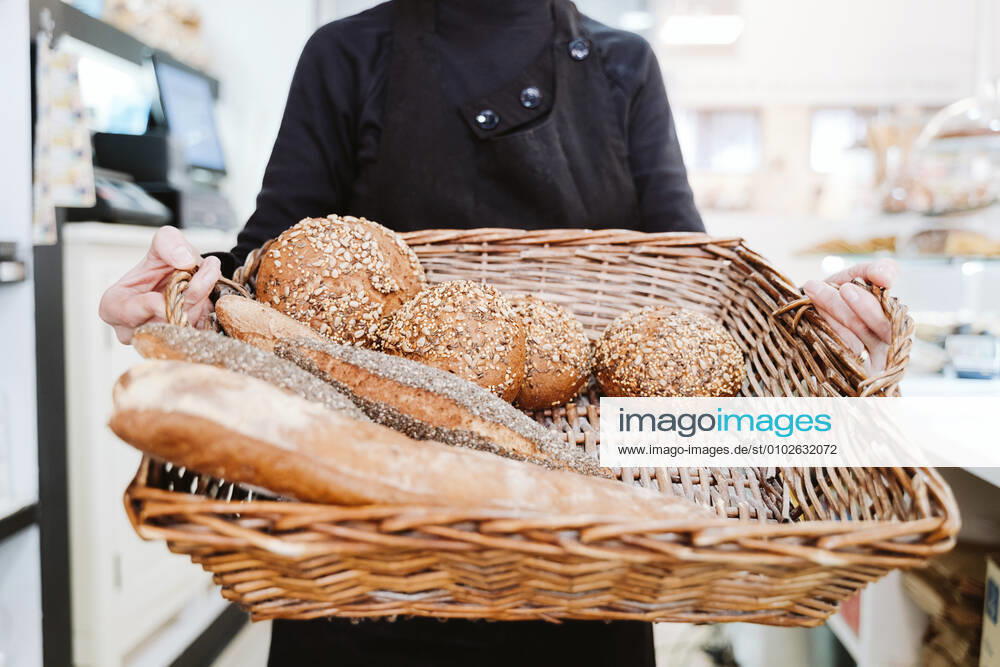 Female baker holding various breads in wicker basket at bakery model released Symbolfoto property released EBBF00399
