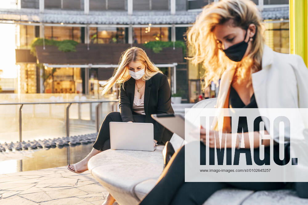 IMAGO Creative: 2022 Aussichten Female entrepreneurs wearing masks working over computers while sitting on seat model released Symbolfoto MEUF01110
