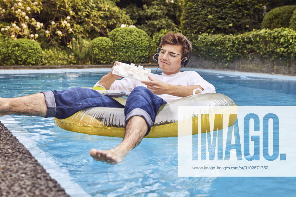 Young man working from home office on airbed in swimming pool looking at architectural model model released Symbolfoto property released UKOF00003