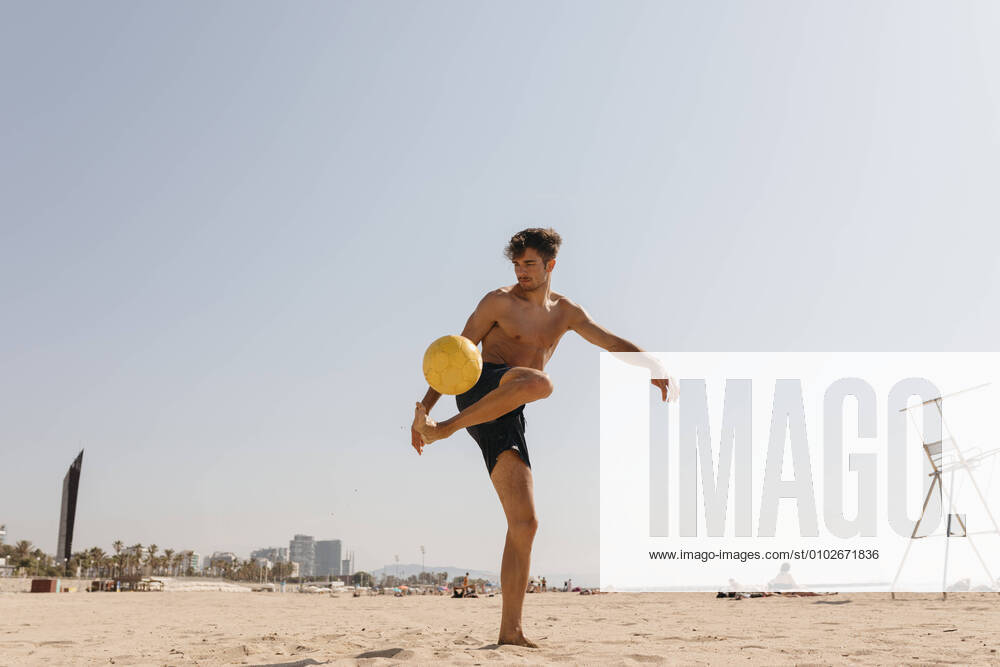 IMAGO Creative: Sommer Sport - Strand Shirtless male athlete playing with ball at beach against clear sky on sunny day model released Symbolfoto VABF03117