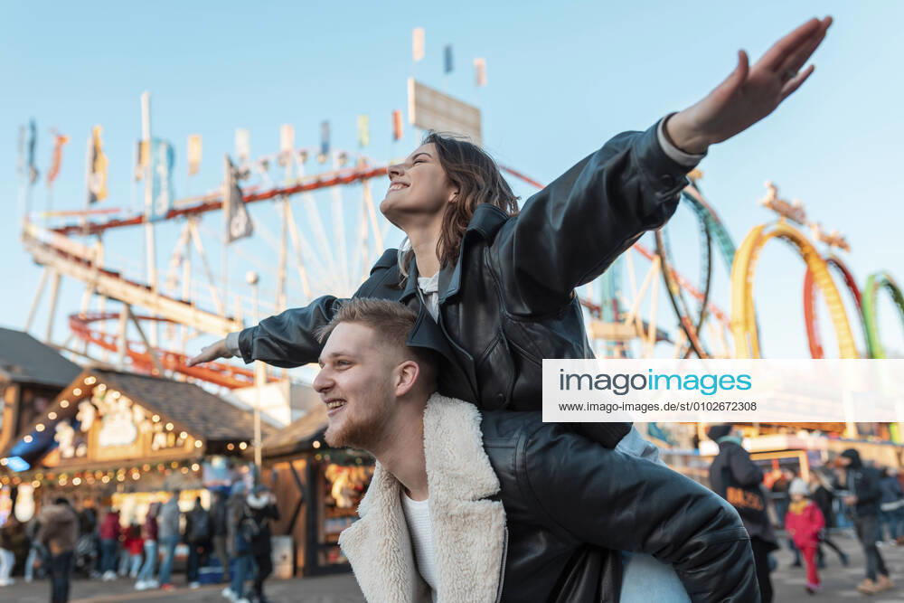 Happy man piggybacking carefree girlfriend while standing at amusement park model released Symbolfoto WPEF03093