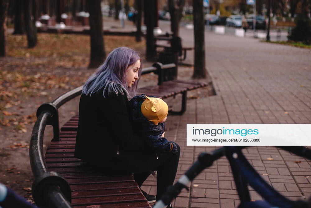 IMAGO Creative: Gesellschaft, Armut Young mother holding baby son while sitting on bench in park CR_DMBE200627-404654-01 ,model released, Symbolfoto
