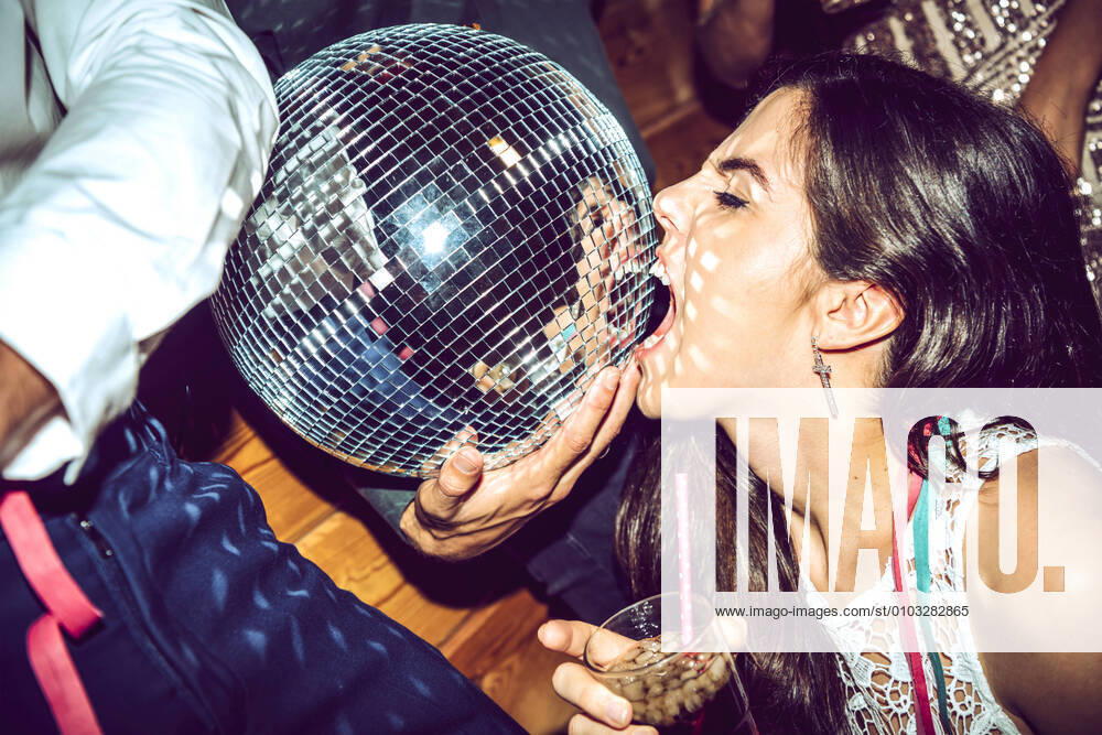 Young woman with eyes closed holding drink and biting disco ball in glamorous party model released Symbolfoto property released EHF00666