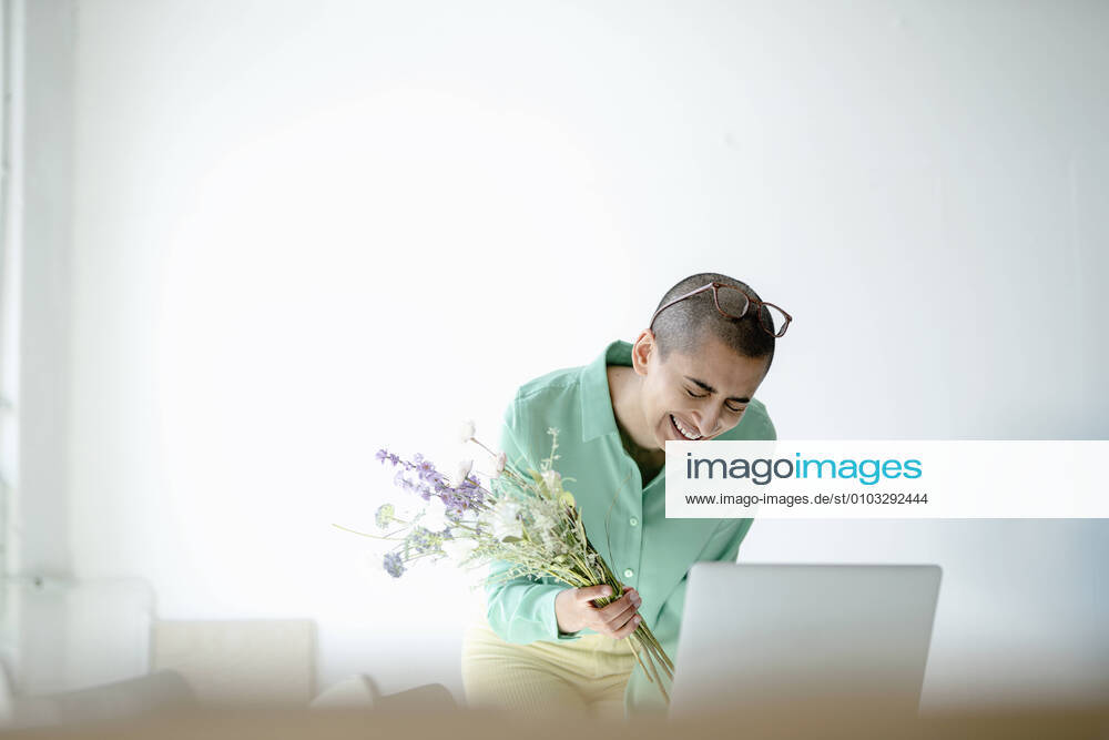 Laughing businesswoman holding bunch of flowers using laptop in loft office model released Symbolfoto property released KNSF08193