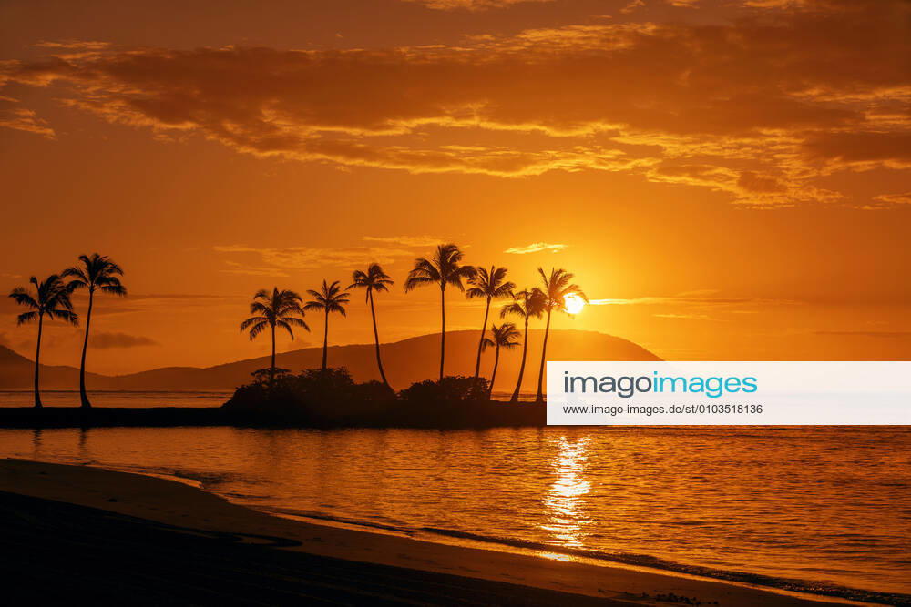 Sunrise at Kahala Beach, WaiÊ»alae Beach Park, with a flare around the sun in a glowing red sky reflected in the tranquil water; Oahu, Hawaii, United States of America