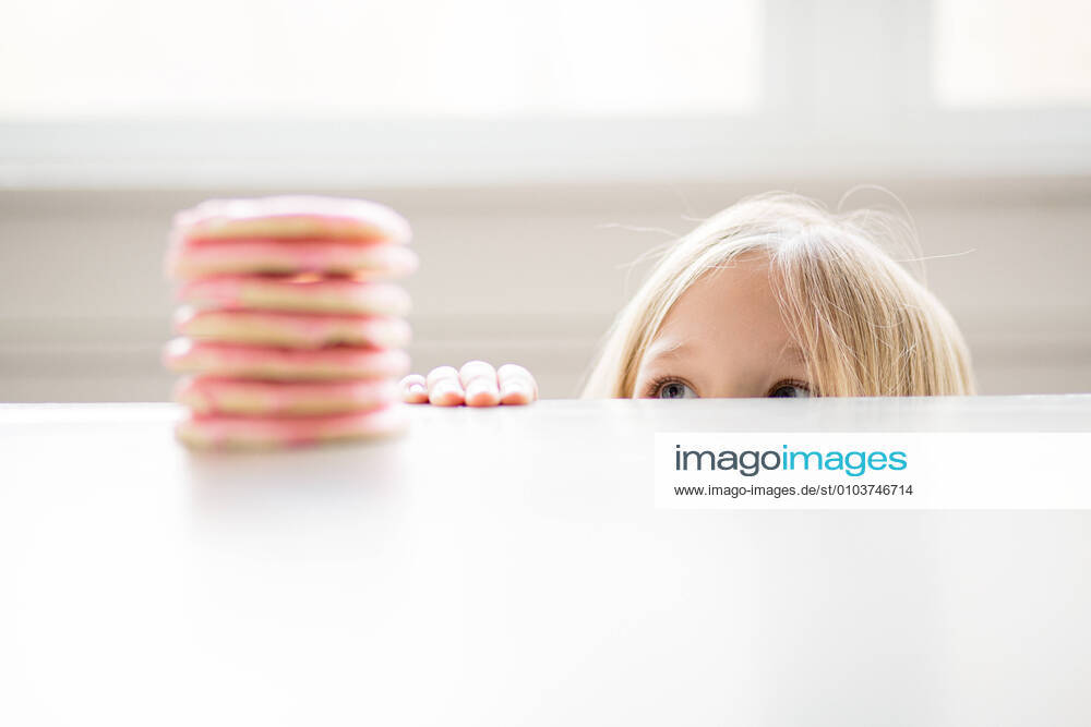 Blond girl peeking at stack of pink frosted sugar cookies on table La Grange Park, IL, United States CR_JERE200828-480987-01 ,model released, Symbolfoto ,property released