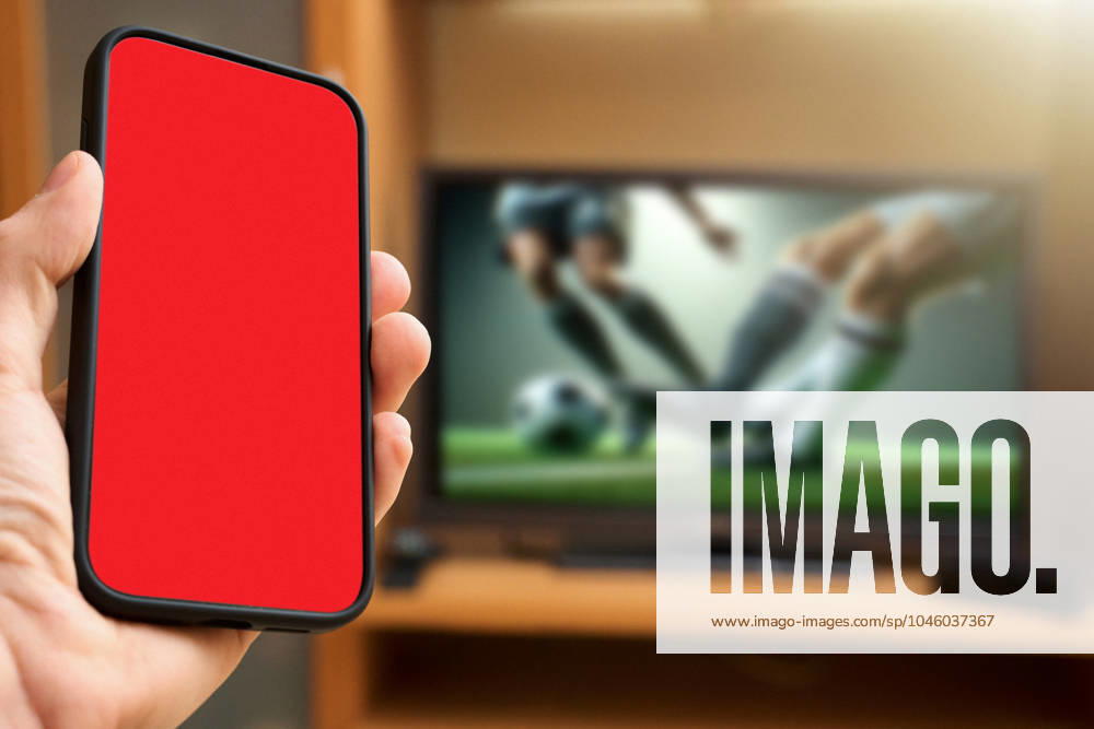 Hand hält Smartphone in der Hand mit einem roten Bildschirm vor einen Fernseher auf dem ein Fußballspiel läuft. Symbolbild Rote Karte im Fußball. FOTOMONTAGE