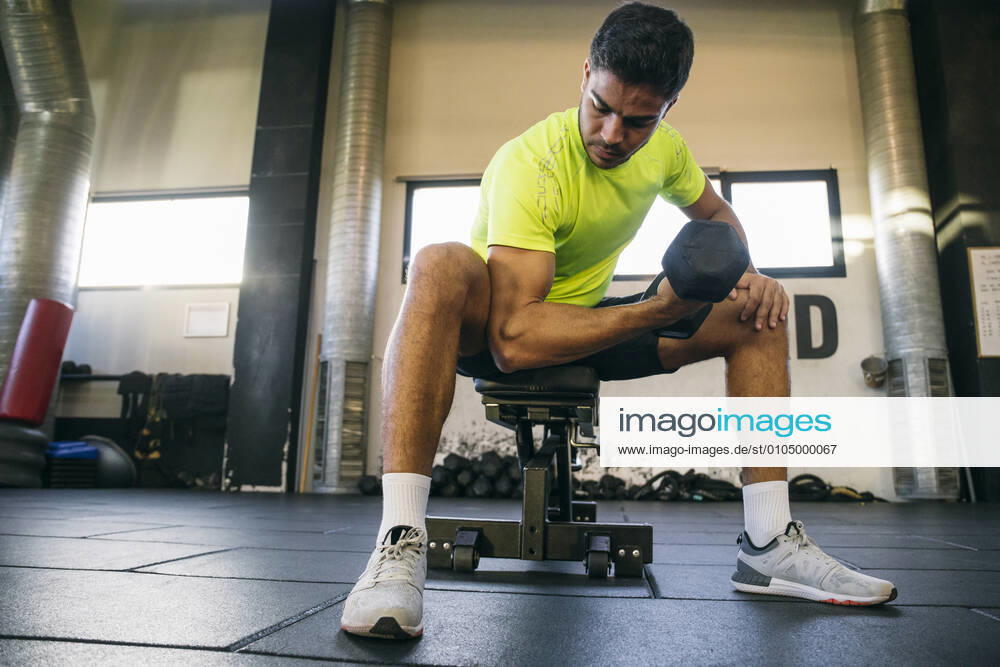 Male athlete lifting dumbbell while sitting in gym model released Symbolfoto property released ABZF03277