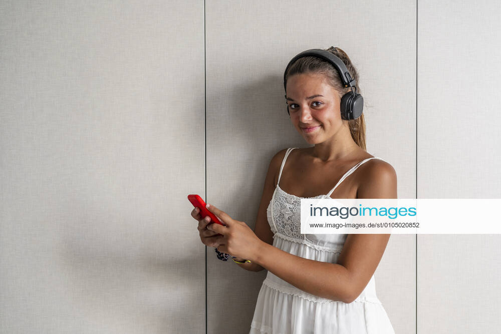 Smiling woman with smart phone standing against closet at home model released Symbolfoto property released DLTSF01177
