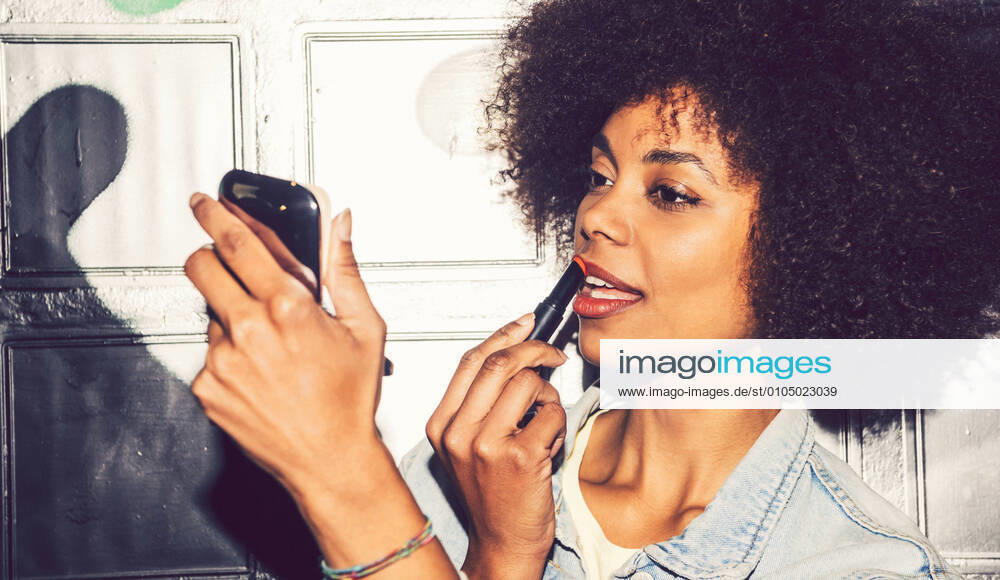 Close-up of woman with curly hair applying lipstick while looking in mirror at night model released Symbolfoto EHF00887