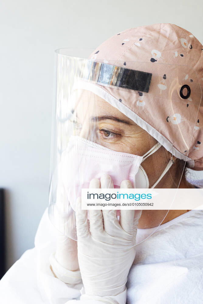 Doctor in protective suit adjusting face mask at office model released Symbolfoto JCMF01279