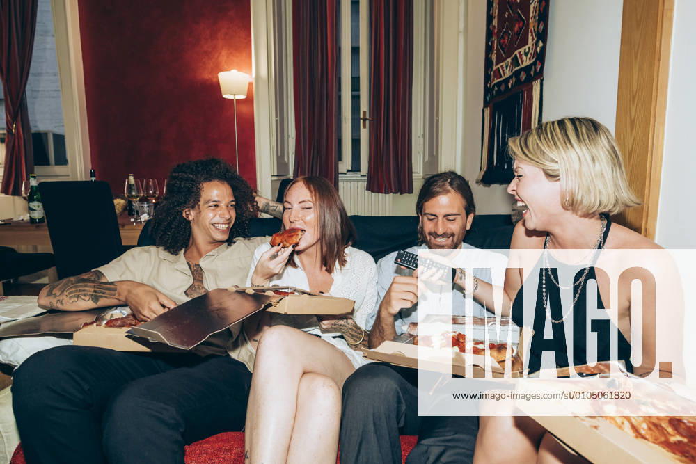 IMAGO Creative, Lifestyle, Leben in einer Wohngemeinschaft, WG Happy friends eating pizza while sitting on sofa in living room model released Symbolfoto property released MEUF01989