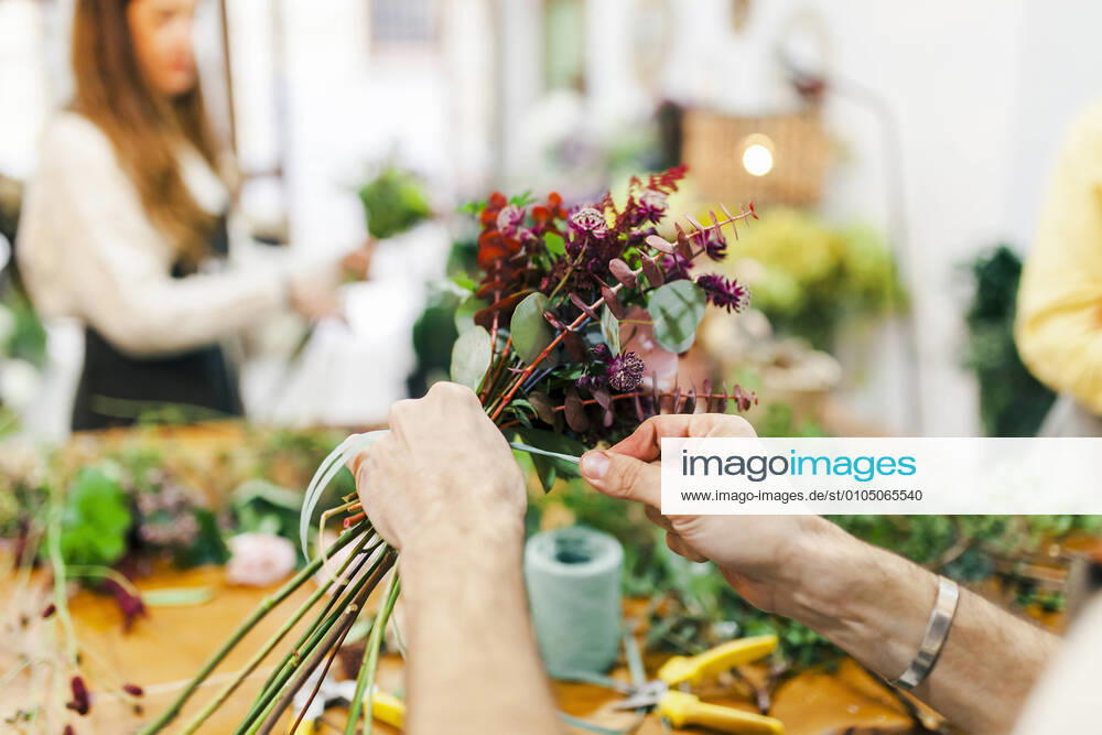 Florist hand tying bunch of flower with team working in background at flower shop model released Symbolfoto property released MRRF00399
