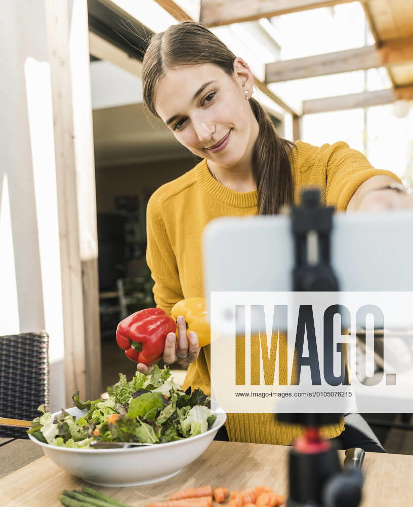 Smiling young woman adjusting smart phone on tripod while filming at home model released Symbolfoto property released UUF21046