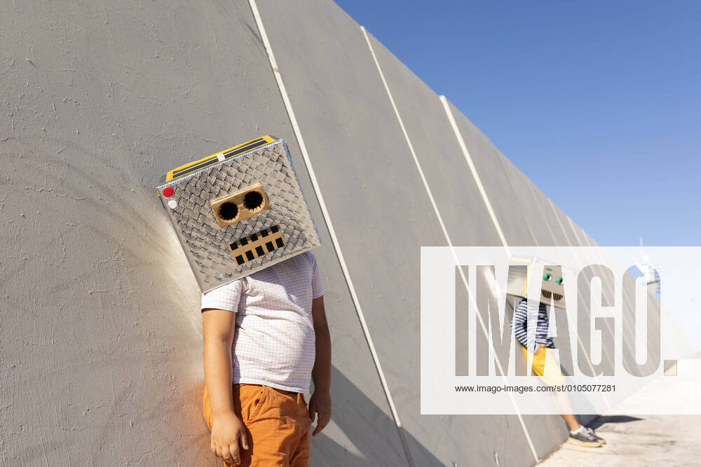 Boys wearing robot masks standing against wall in city on sunny day model released Symbolfoto VABF03132
