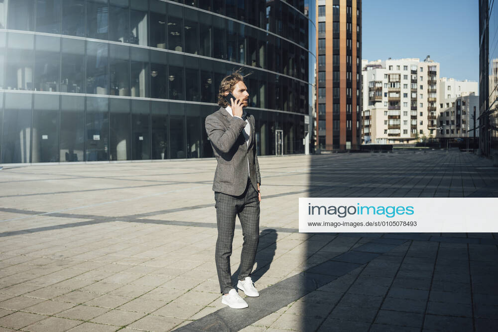 Male entrepreneur talking on smart phone while looking away at financial district during sunny day model released Symbolfoto VPIF02900