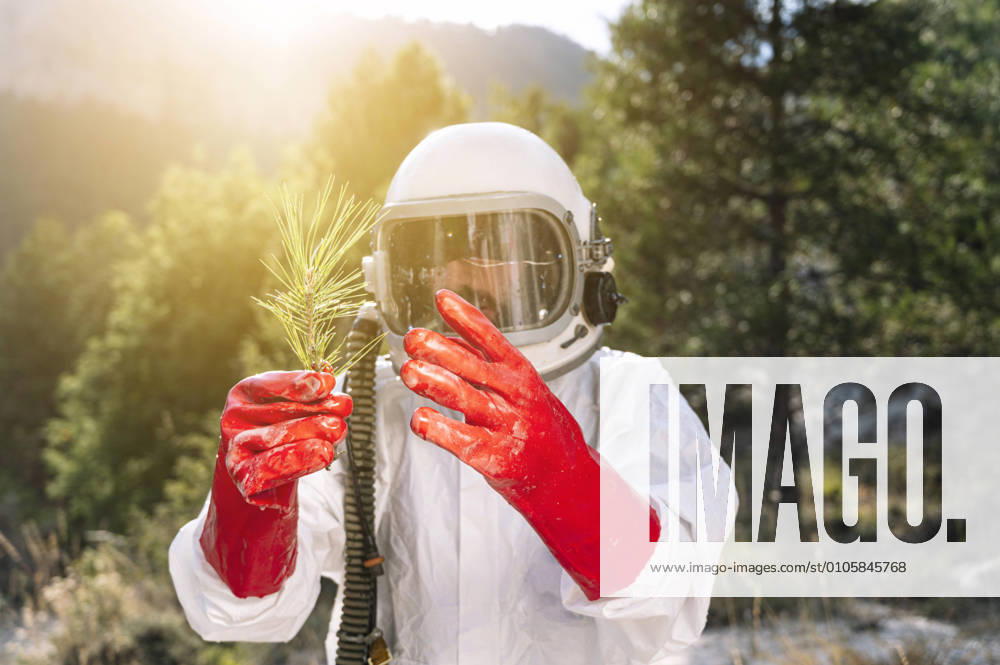 IMAGO Creative: Klimawandel - Zukunft und Innovation Close-up of male astronaut holding plant while standing against trees model released Symbolfoto JCMF01434