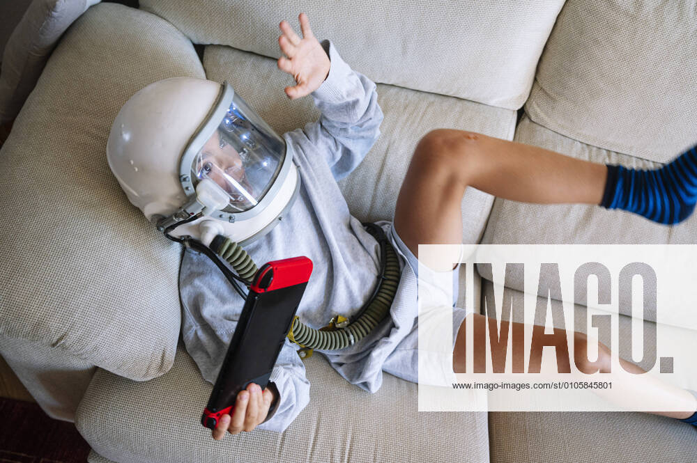 Boy wearing space helmet gesturing while playing video game sofa at home model released Symbolfoto property released JCMF01459