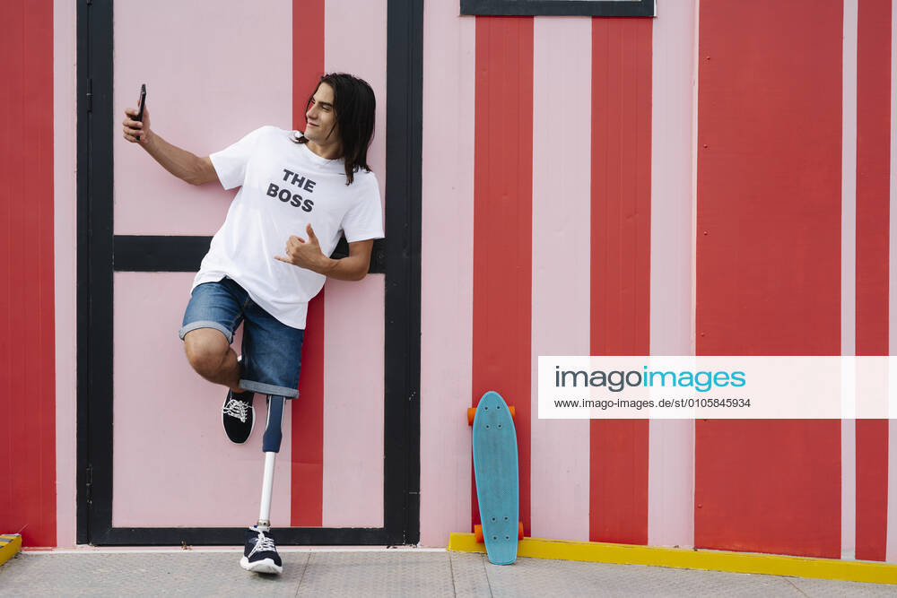 Disabled man taking selfie while standing against red wall model released Symbolfoto JCZF00315