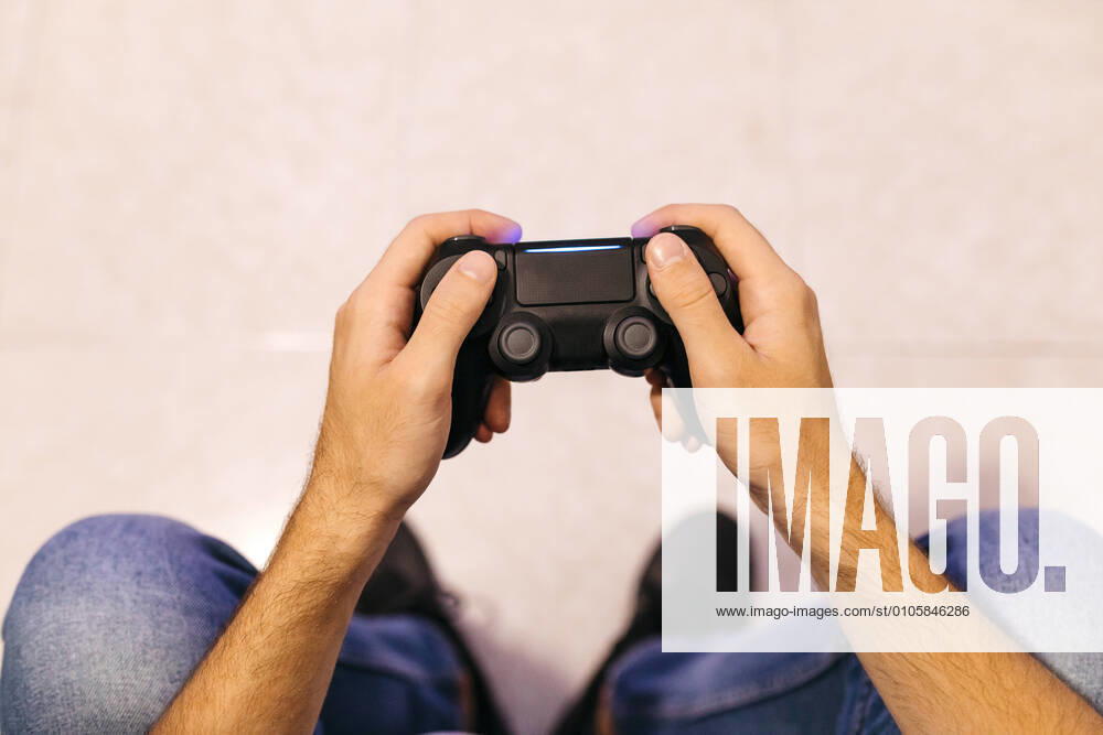 IMAGO Creative, Lifestyle, Gaming Young male gamer holding controller while playing at home model released Symbolfoto property released JRFF04749