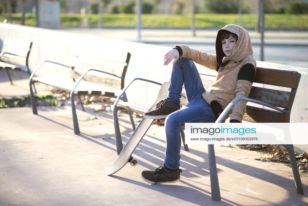 Young hooded boy sitting on bench next his skateboard, looking camera Granollers, CT, Spain CR_RAFE201110C-525488-01 ,model released, Symbolfoto