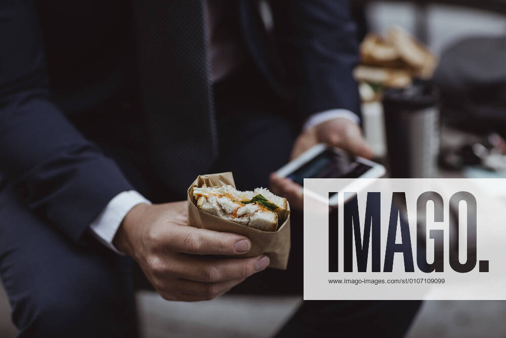 Midsection of entrepreneur with smart phone and sandwich sitting in city, MA82399, Sweden, Stockholm, model released