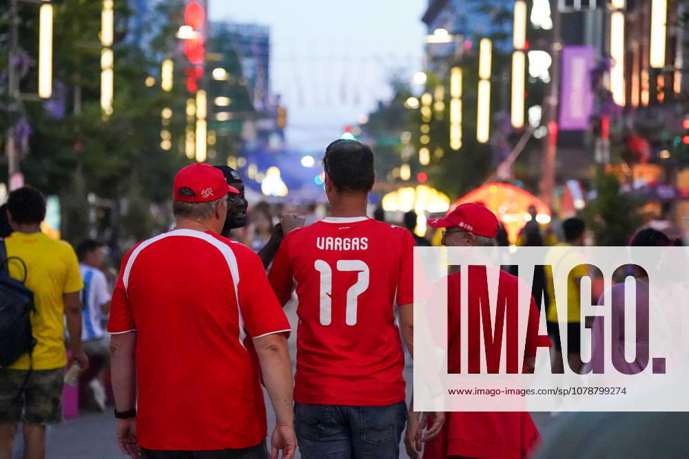 Canada Soccer 2026 FIFA World Cup Group Stage Switzerland vs. Canada BC Place Stadium Vancouver, British Columbia Swiss soccer fans in red jerseys and fan apparel on a bustling pedestrian street in the evening, rear view, jersey with Vargas 17 on it, fan march, fan culture, supporters of the Swiss national team, public viewing atmosphere, leisure, travel, tourism, crowd, street life, twilight, bokeh lights, soccer enthusiasm, supporters, away fans, impression, symbolic photo