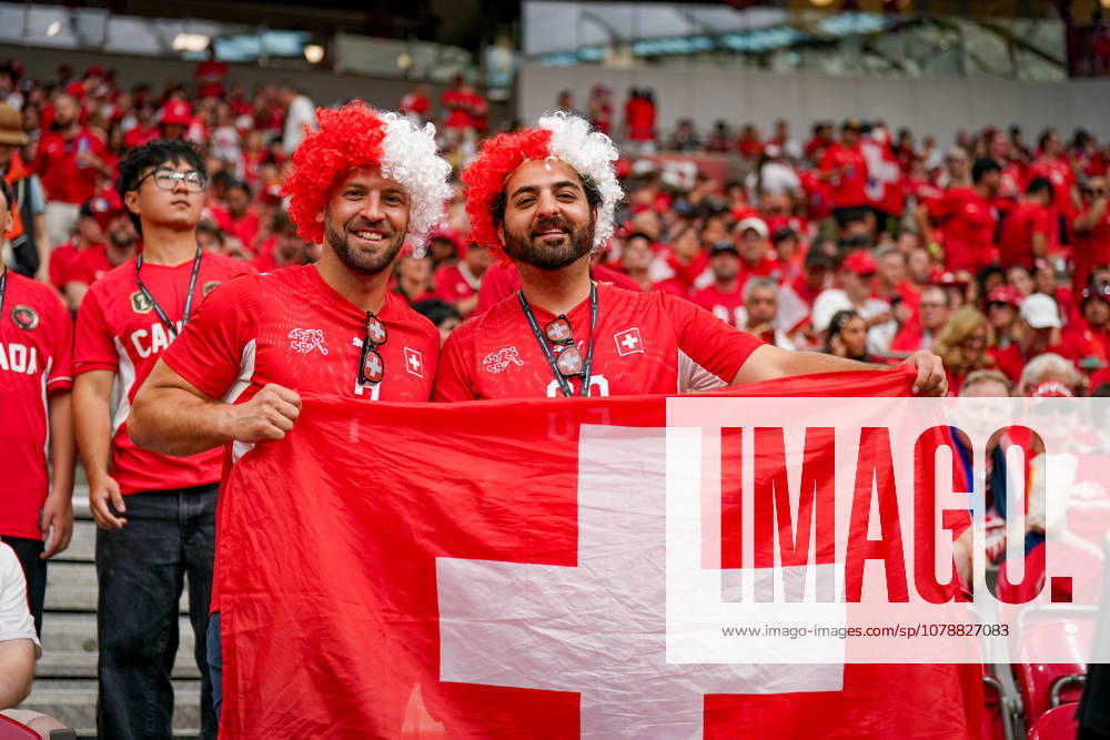 Canada Soccer 2026 FIFA World Cup Group Stage Switzerland vs. Canada BC Place Stadium Vancouver, British Columbia Swiss soccer fans, supporters, fan portrait, two supporters with a Swiss flag, Swiss national flag, red and white wigs, SFV jersey, Swiss Football Association, facial expression, smile, fan culture, soccer enthusiasm, spectators, stands, stadium atmosphere, fan section, supporters, cheering, international fans, group photo, portrait, flag, national pride, sporting event, World Cup atmosphere, audience, leisure, crowd, Switzerland, soccer, emotions, red fan apparel